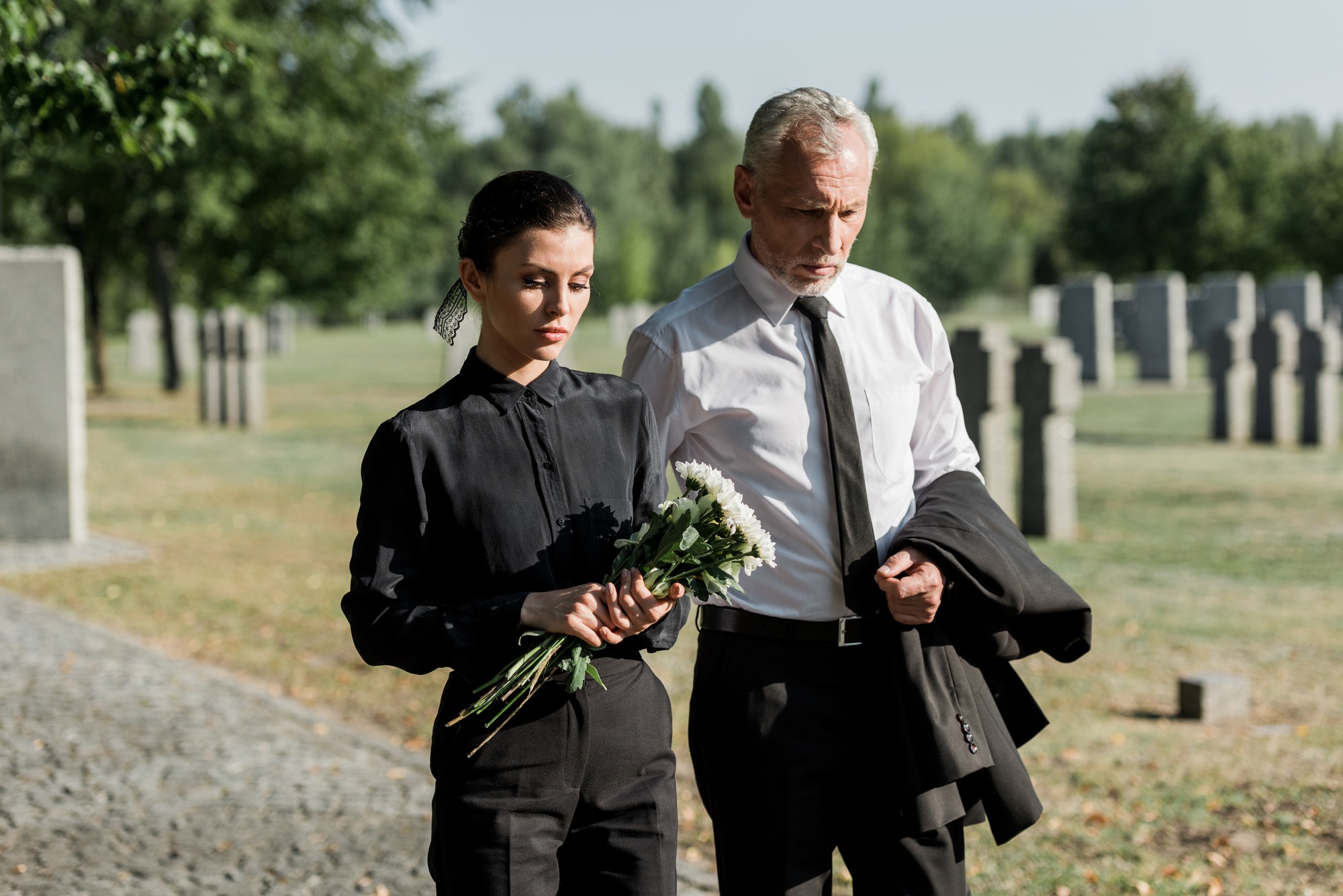 bearded-senior-man-walking-near-woman-with-flowers-on-funeral.jpg